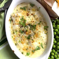 a white bowl filled with food next to green peas and bread on top of a table