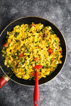 a pan filled with rice and vegetables on top of a gray counter next to a red spatula