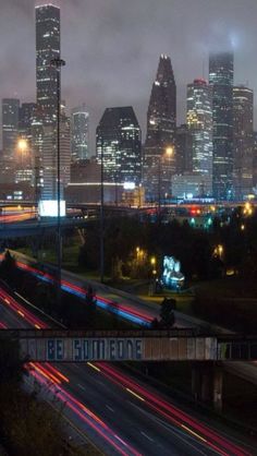 the city skyline is lit up at night, with long exposure lights streaking across the street