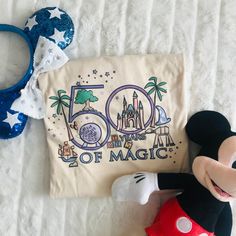 a mickey mouse laying on top of a bed next to a bag with the word 50 years of magic written on it