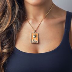 a woman wearing a necklace with an orange and white square pendant hanging from it's center