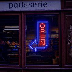 a neon sign that reads open in front of a store window with an arrow pointing to the right