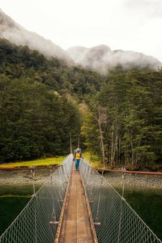 a man walking across a suspension bridge over a river