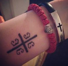 a close up of a person wearing a bracelet with a cross tattoo on their arm