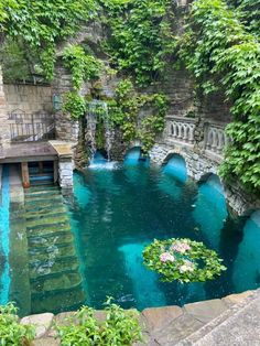 an outdoor swimming pool surrounded by greenery and stone steps leading up to the water