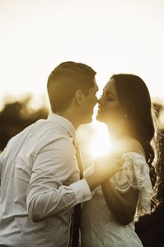 a bride and groom kissing in front of the sun