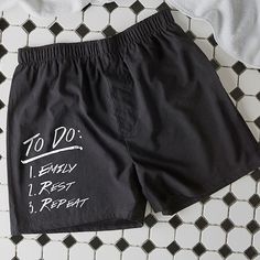 a pair of black shorts with white writing on them sitting on a tiled floor next to a pillow