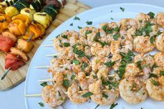 several skewers of shrimp and vegetables on a white plate next to a cutting board