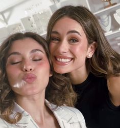 two beautiful women standing next to each other with their eyes closed and one blowing bubbles in the air