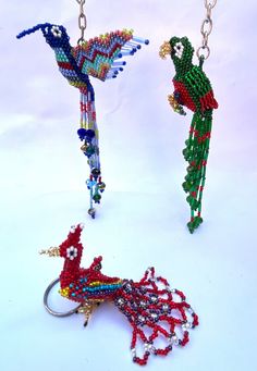 three different types of beaded key chains on a white surface with one bird hanging from the chain