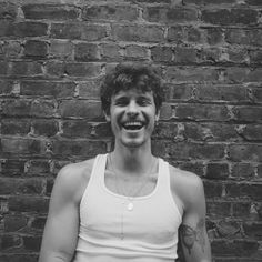 black and white photograph of a man smiling in front of a brick wall with his arms crossed