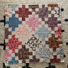 an old quilt is laying on the floor in front of a white rug with black and red squares