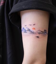 a woman with a tattoo on her arm that has mountains and birds flying in the sky