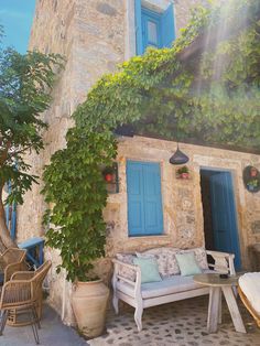 an old stone house with blue shutters and green vines on the outside, along with wicker furniture