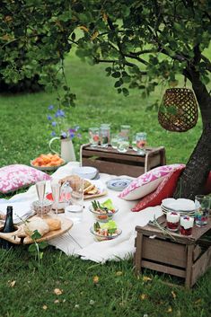 a picnic table with food and drinks on it in front of some flowers, grass and bushes