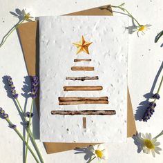 a card with a christmas tree made out of sticks and stars on it, surrounded by wildflowers