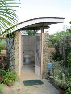 an outdoor toilet in the middle of some plants and trees with a door open to it