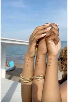 two women with matching tattoos on their arms holding each other's hands in front of the ocean