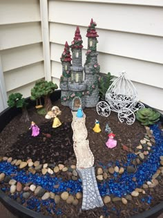 a fairy garden in a pot with blue rocks and gravel around it, including a statue of a castle