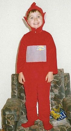 a young boy in a red costume standing next to a couch