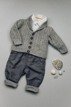 a baby's sweater and pants are laid out next to some seashells