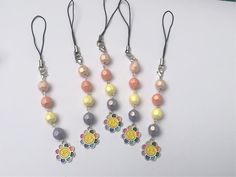 four necklaces with flowers and beads hanging from hooks on a white surface, next to a pair of scissors