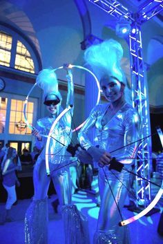 two women dressed in silver and white are performing with hoop rings on their heads at an event