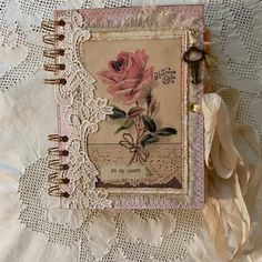 an altered book with a pink rose on the cover is laying on lace covered fabric