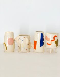 three ceramic mugs with designs on them sitting next to each other in front of a white wall