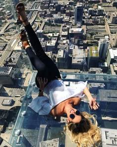 a woman is hanging upside down on the glass floor in front of an urban cityscape