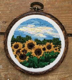 an embroidered sunflower patch hanging from a wooden frame on a wood table with a metal hook