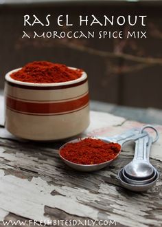 a wooden table topped with a bowl filled with red powder next to a measuring spoon