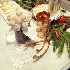 a table topped with lots of desserts on top of a white counter covered in pine cones