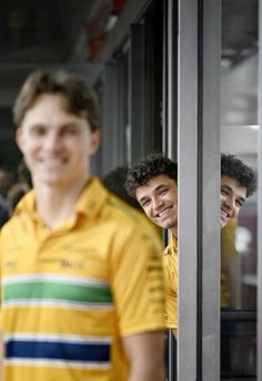 three young men standing next to each other in front of a glass door with the reflection of another man's face