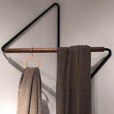 a pair of brown towels hanging on a clothes rack next to a white wall with a wooden hanger