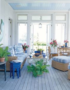 a living room filled with lots of furniture and plants on top of wooden flooring