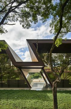 an open air pavilion with trees in the foreground and grass on the other side