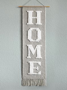 a white wall hanging with the words home on it and fringes attached to it