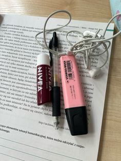 three different types of lipstick sitting on top of an open book next to headphones