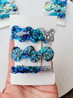 someone is holding three hair clips in their hand with blue and silver sequins on them