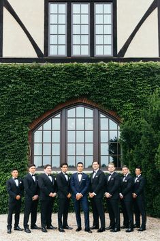 a group of men standing next to each other in front of a building with ivy growing on it