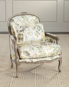 an ornate chair with floral upholstered fabric on the back and arms, sitting in front of a white paneled wall