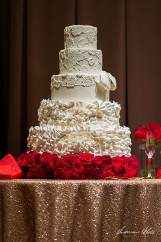 a wedding cake sitting on top of a table next to red roses and wine glasses