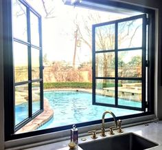 an empty swimming pool is seen through the open window in this kitchen sink and countertop