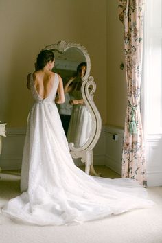 a woman standing in front of a mirror wearing a wedding dress