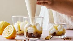 a person pouring cream into some desserts in glasses with lemon wedges on the side