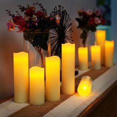 many lit candles on a table with flowers in the background