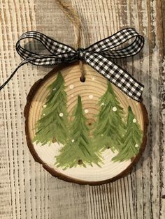 a wooden ornament with pine trees painted on it and a ribbon tied around the top