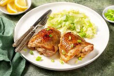 two pieces of chicken on a white plate with green salad and silverware next to it