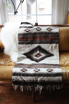 a couch with a blanket on top of it in front of a window and a lamp